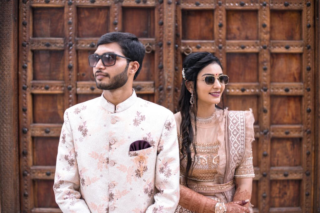 Stylish Indian couple in traditional attire posing in front of ornate wooden doors.